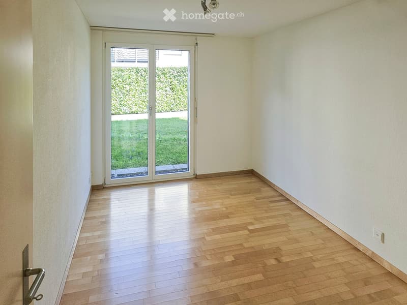 Empty room with wooden flooring, white walls, and a large sliding glass door leading to a green outdoor area.