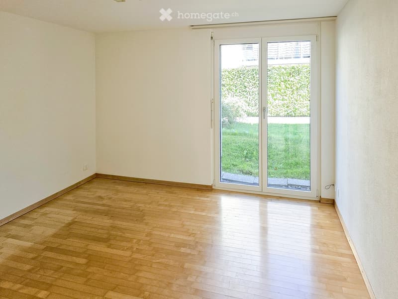 Empty room with wooden flooring and large sliding glass doors leading to a green outdoor area.