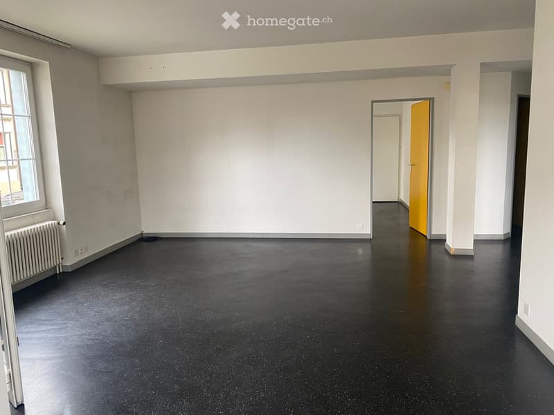 Empty room with white walls, black polished floor, radiator, and a doorway leading to another room.
