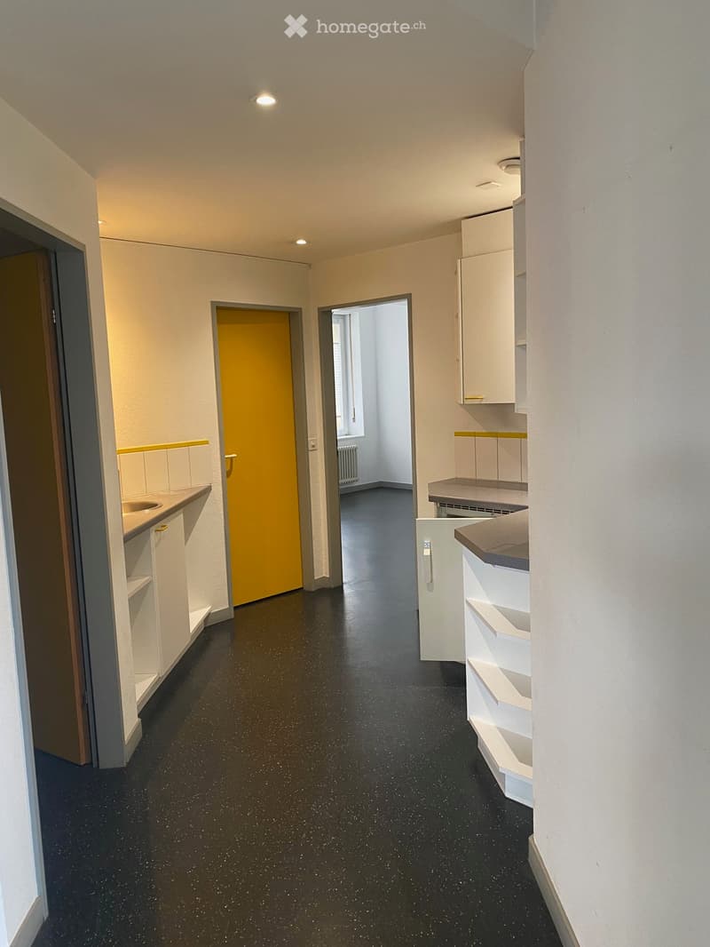 Empty hallway with black speckled flooring, white walls, and several doors leading to different rooms.