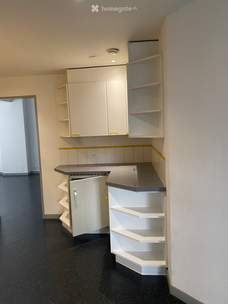 Empty room with white cabinets, shelves, and a black speckled floor. No furniture or personal items are present.
