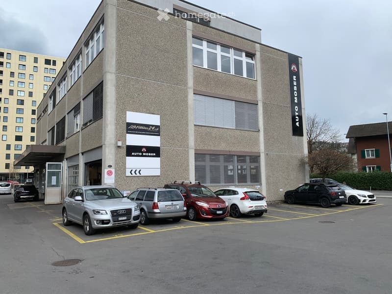 Multi-story building with signage for 'AUTO MOSER' and 'LifeFitness 24.ch', with several parked cars in front.