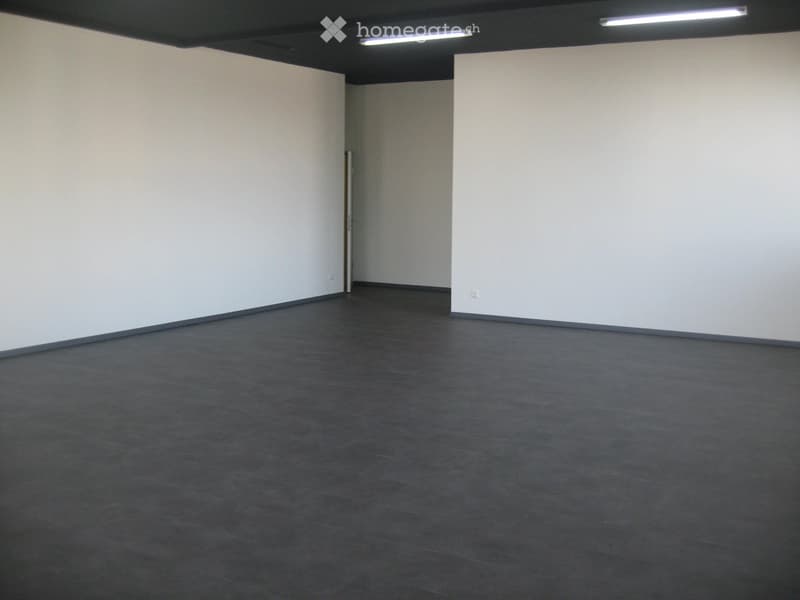 Empty room with white walls, dark tiled floor, and a single door leading to another space.