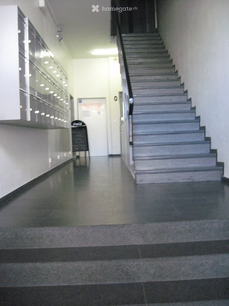 Modern hallway with a staircase, glass wall, and a Coca-Cola sign on the floor.