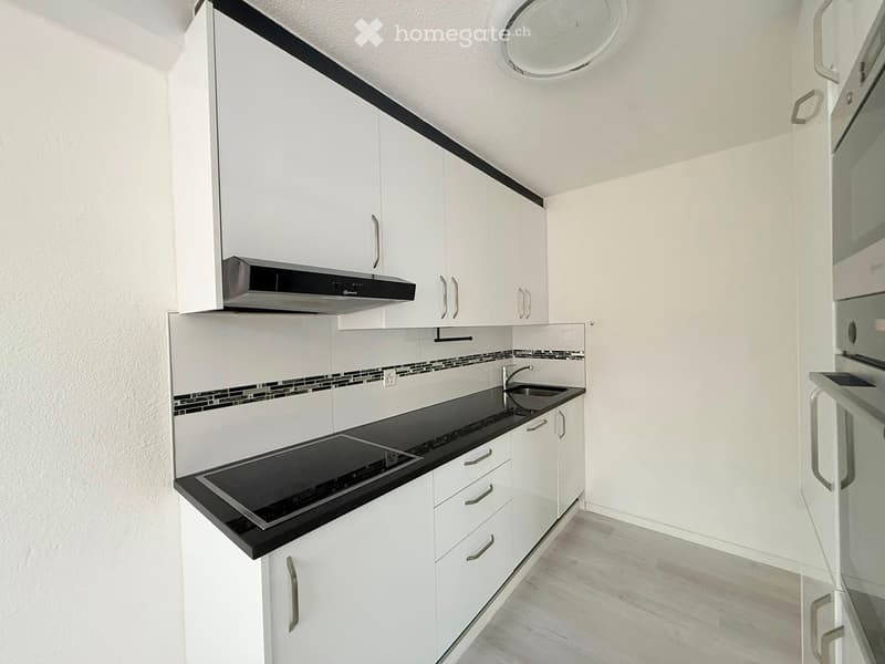 Modern kitchen with white cabinets, black countertop, built-in stove, and sink.