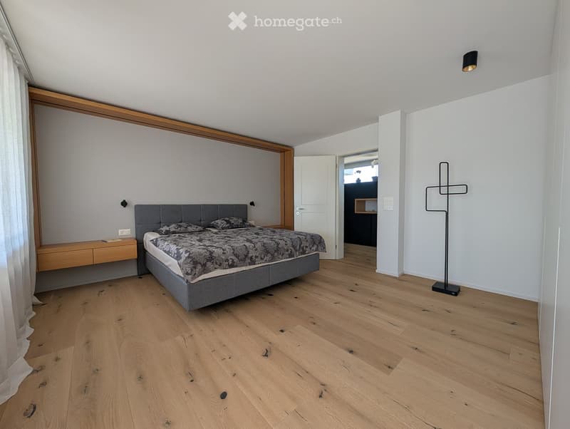 Modern bedroom with wooden flooring, grey upholstered bed, nightstand, and coat rack.