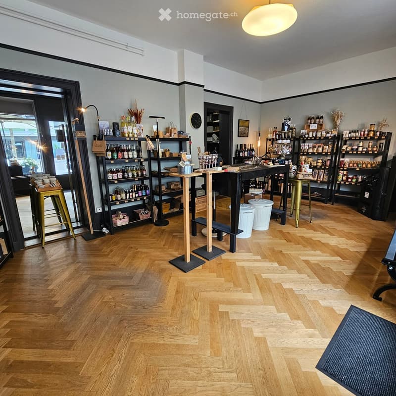 A well-lit, modern retail space with wooden flooring, shelves stocked with various products, and several stools and tables arranged for display and seating.