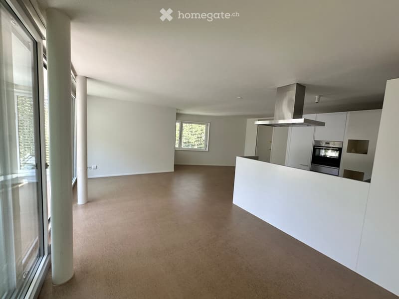 Empty kitchen with white cabinets, stainless steel appliances, and a white countertop. The space features large windows and a neutral color palette.