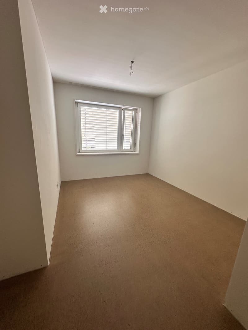 Empty room with beige walls, carpeted floor, and a single window with white blinds.