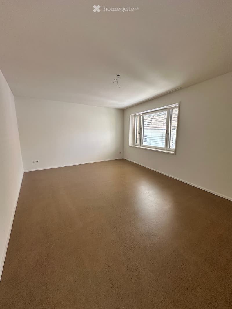 Empty room with beige walls, a single window with blinds, and a smooth concrete floor.