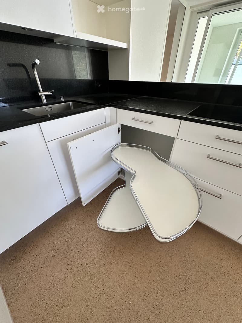 Modern kitchen with white cabinets, black countertops, a stainless steel sink, and a white stool tucked under the counter.