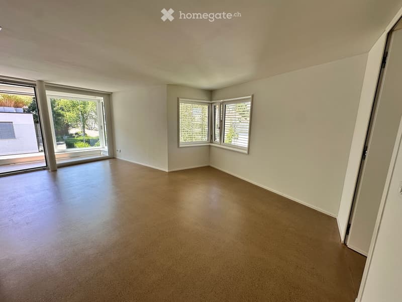 Empty room with light-colored walls, polished concrete floor, large windows, and sliding glass door leading to outdoor area.