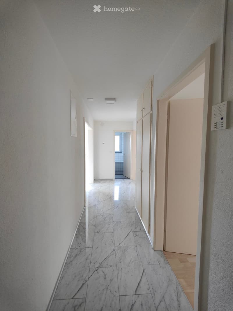 Empty hallway with marble flooring, white walls, and several doors leading to other rooms.