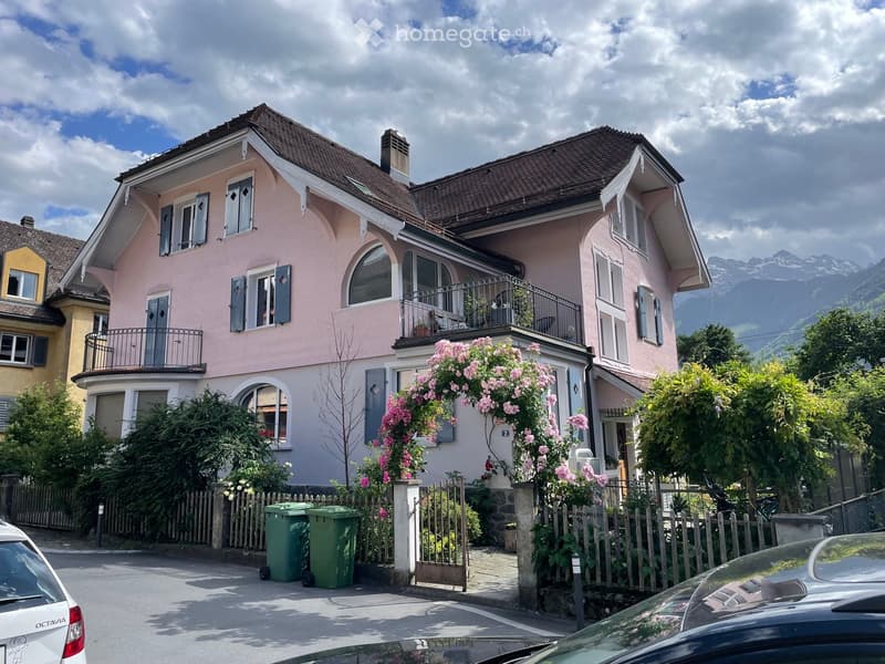 Two-story pink house with white trim, multiple windows, balconies, and a view of mountains in the background.