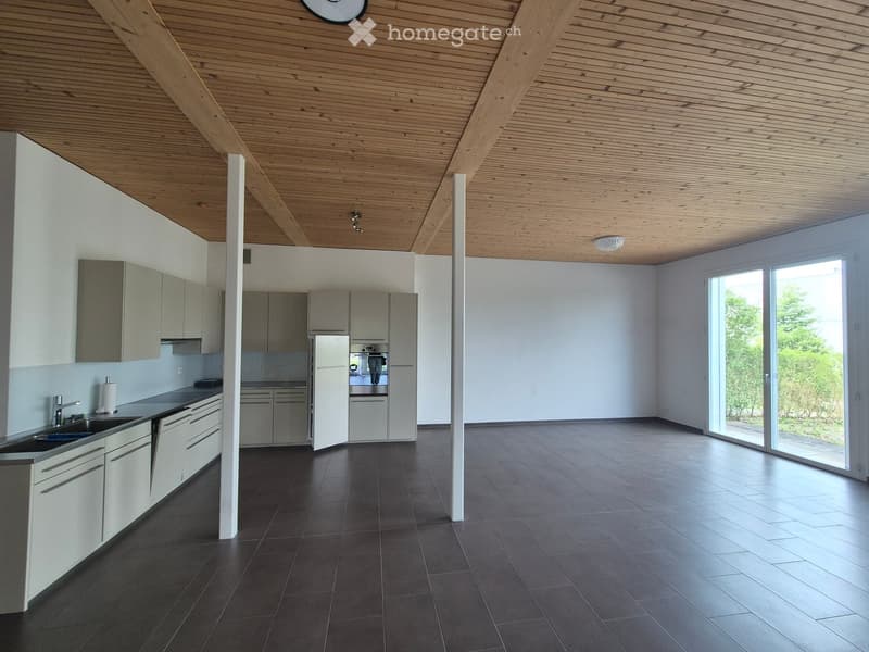 Modern kitchen with sleek grey cabinets, dark tiled floor, and large windows. Features a sink, faucet, refrigerator, and oven.