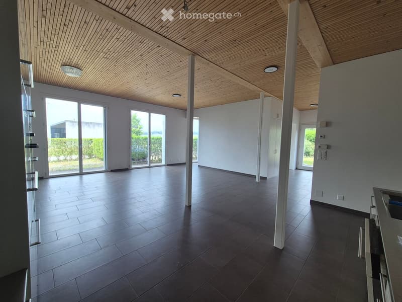 Open, unfurnished room with dark tiled flooring, white walls, large sliding glass doors leading to an outdoor area, and a wooden slanted ceiling with recessed lighting.