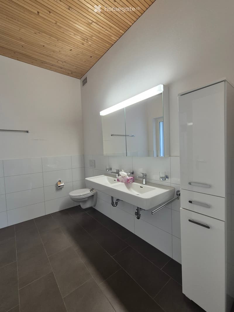 Modern bathroom with a white sink, toilet, large mirror with built-in lighting, and white cabinetry.