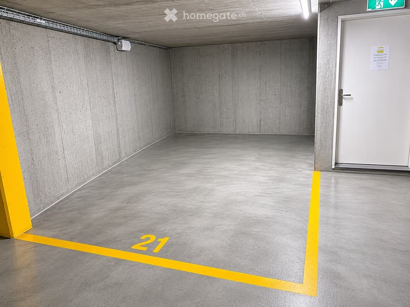Empty parking space with concrete walls and floor, marked with yellow lines and numbered '21'.