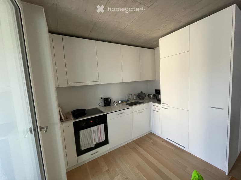 Modern kitchen with white cabinets, wooden flooring, and stainless steel appliances including an oven, sink, and coffee maker.