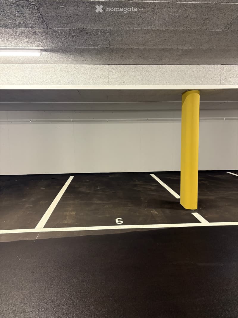 Empty underground parking space with marked parking spot number 6, yellow support pillar, and clean concrete floor.