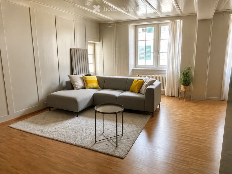 Modern living room with grey sectional sofa, yellow throw pillows, round coffee table, and a potted plant near the window.