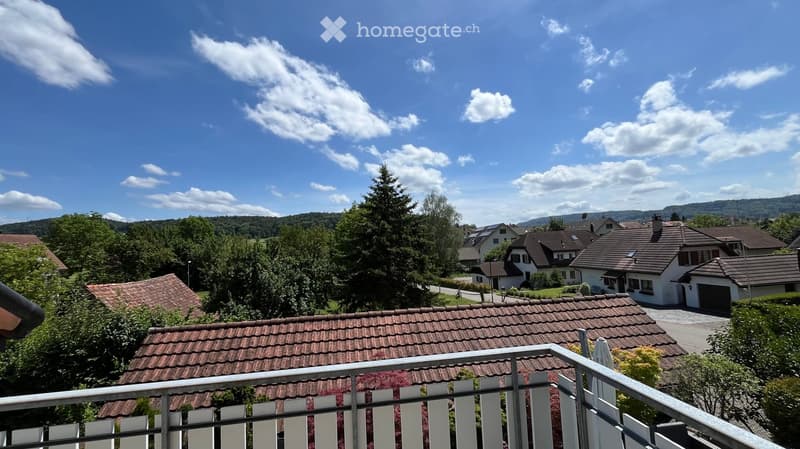 Balcony overlooking a residential neighborhood with houses, trees, and a clear blue sky.