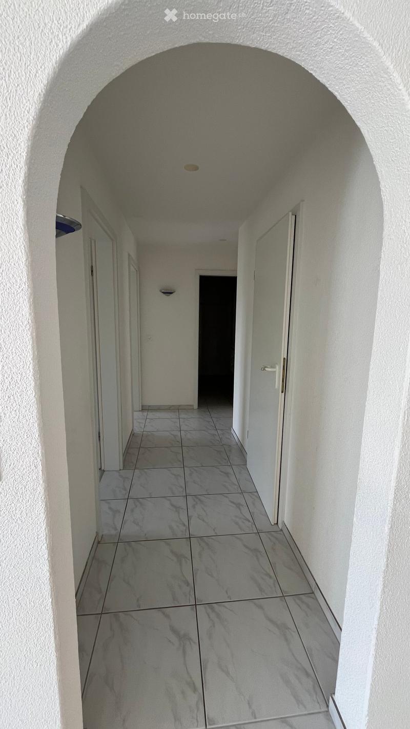 A narrow, arched corridor with white walls and a tiled floor, featuring recessed lighting and doors on both sides.