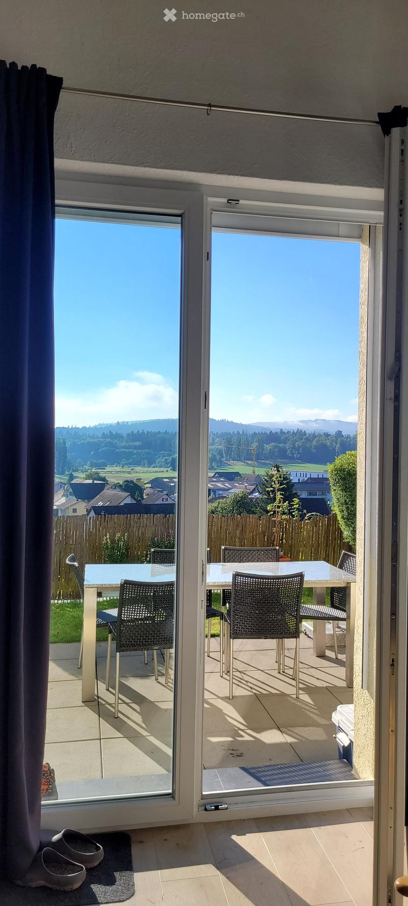 Balcony with large glass doors opening to a scenic view, featuring a table and chairs.