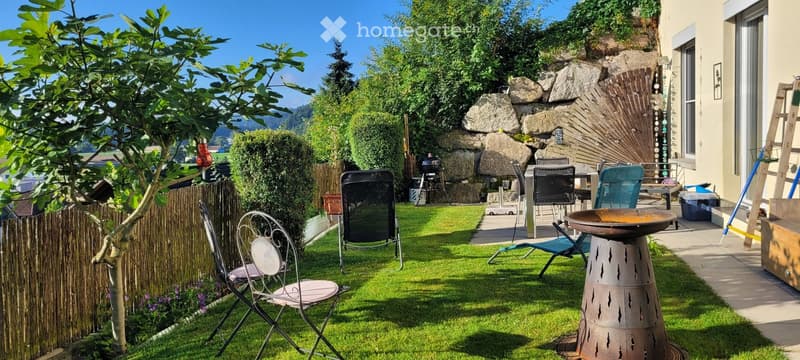 Well-maintained garden with a stone wall, barbecue, outdoor seating area, and decorative elements.
