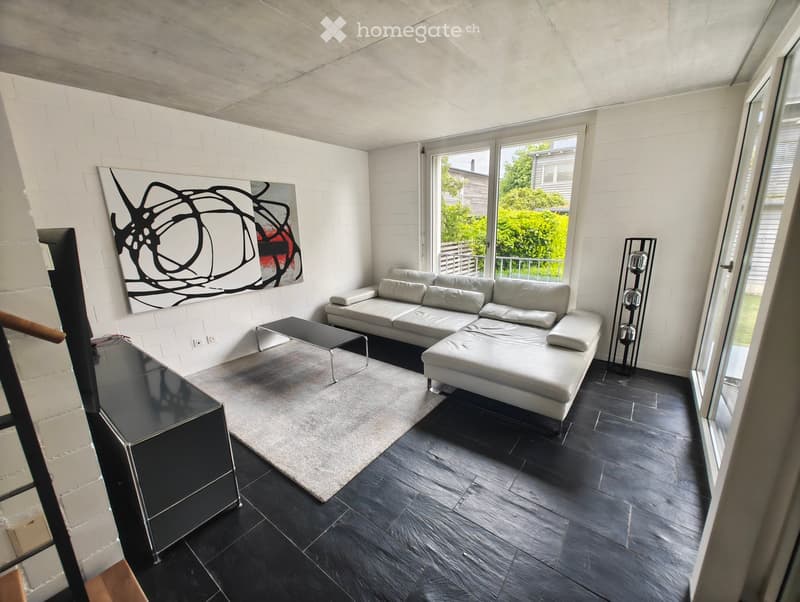Modern living room with white brick walls, dark wooden flooring, a white sectional sofa, a glass coffee table, a floor lamp, and a large abstract painting on the wall.