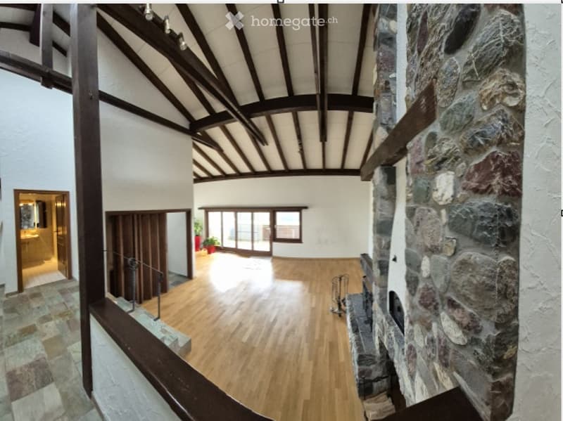 Open-plan space with wooden flooring, exposed wooden beams, large windows, and a stone fireplace. No furniture or equipment visible.