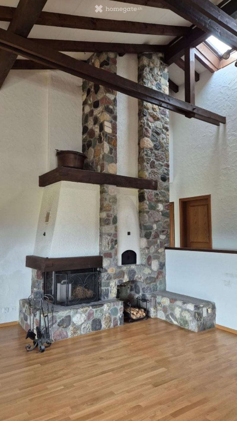 Empty room with exposed wooden beams, a stone fireplace, and wooden flooring.