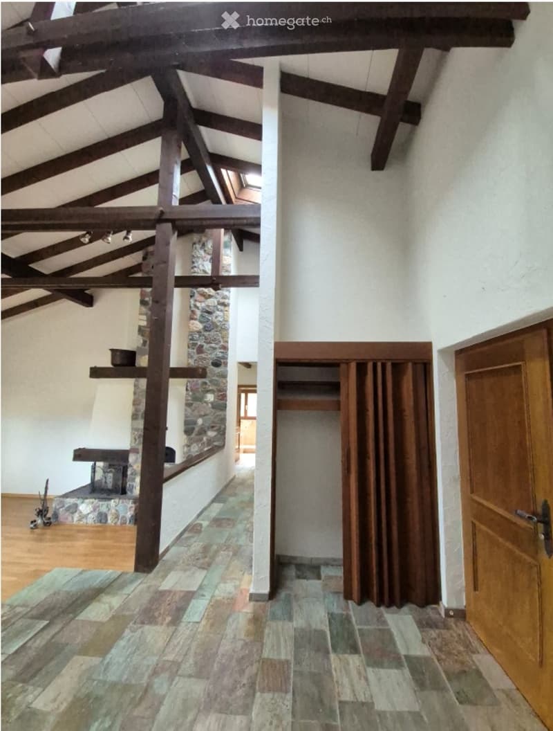 Spacious hallway with exposed wooden beams, stone fireplace, wooden doors, and tiled flooring.