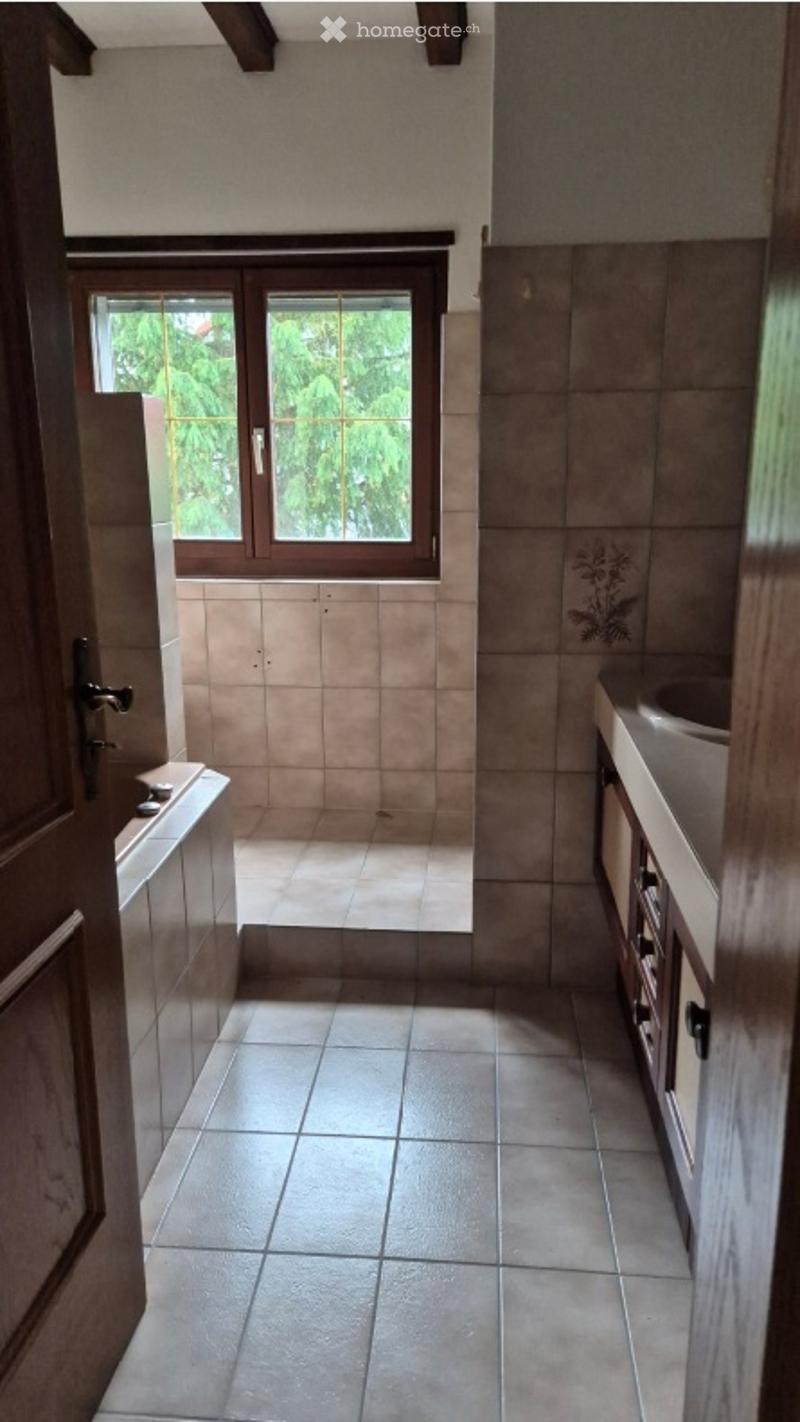 Bathroom with beige tiles, a bathtub, a sink with a wooden cabinet, and a window overlooking greenery.