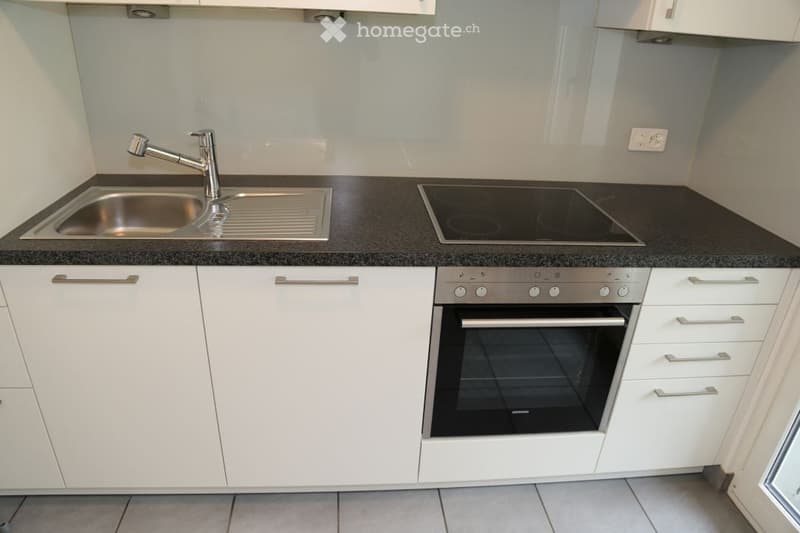 Modern kitchen with white cabinets, black countertop, stainless steel sink and faucet, induction cooktop, and built-in oven.