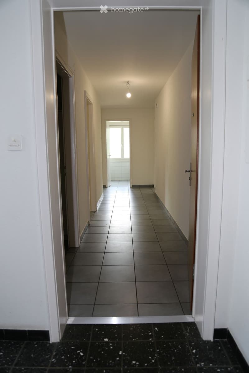 Empty hallway with tiled floors, white walls, and several doors leading to other rooms.