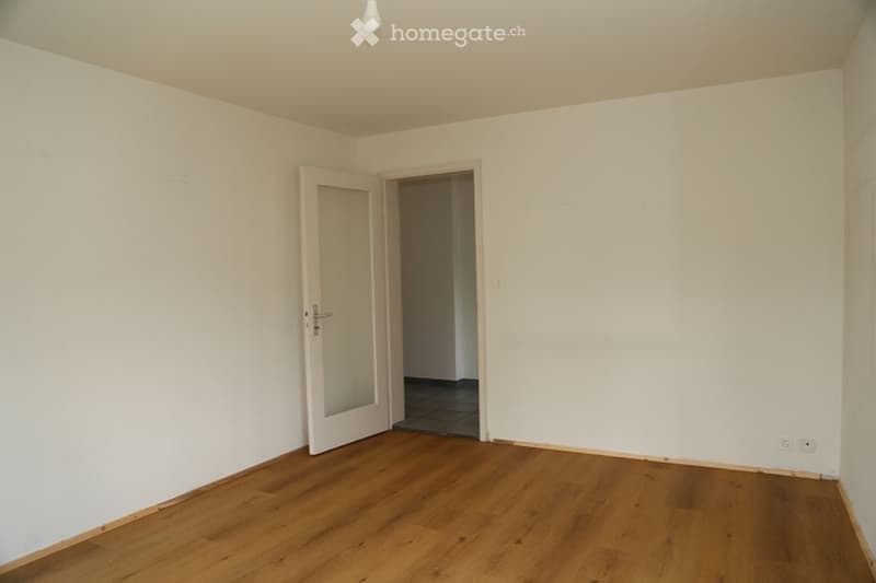 Empty room with wooden flooring, white walls, and a single door leading to another space.