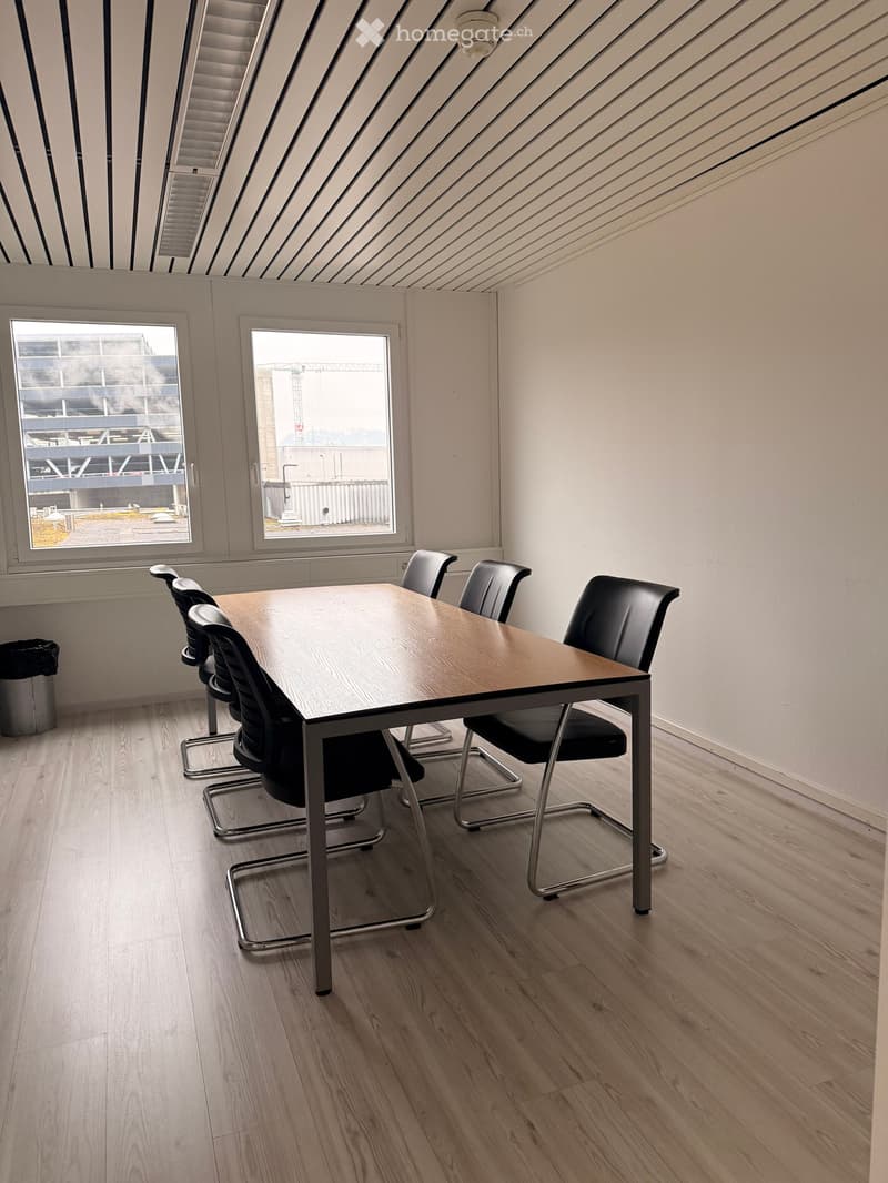Wooden table, black chairs, wooden flooring, large windows, trash bin