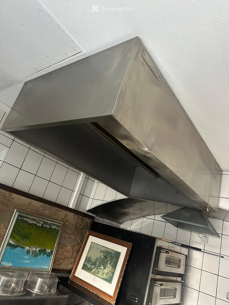 Stainless steel range hood above a kitchen counter with framed pictures and casserole dishes on the counter.