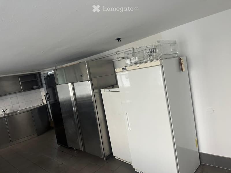 Commercial kitchen with stainless steel appliances, including multiple refrigerators, a sink, and cabinets.