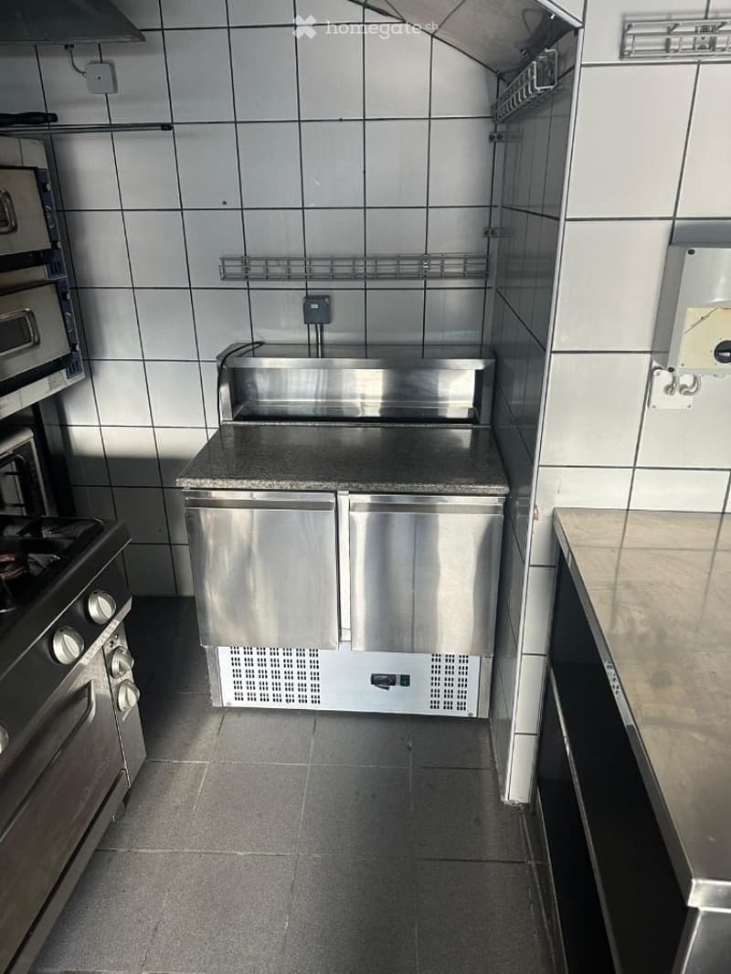 Commercial kitchen with stainless steel appliances, granite countertop, and tiled walls.
