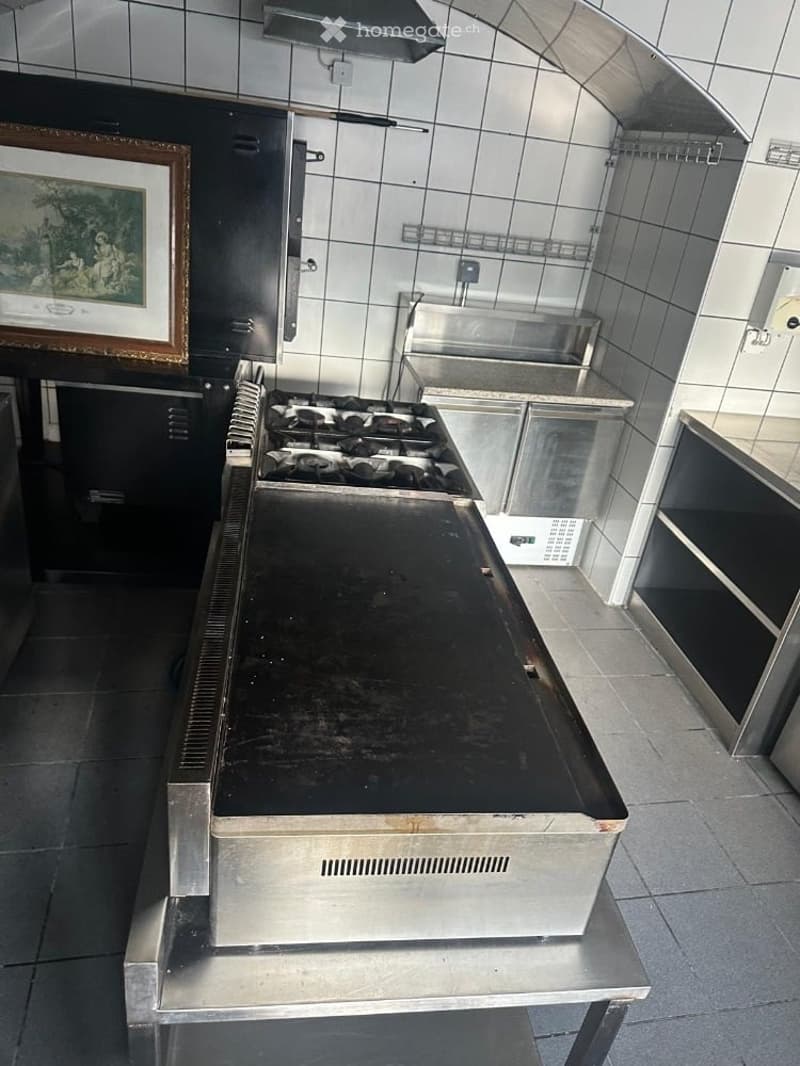 Commercial kitchen with stainless steel appliances, including a stove, griddle, fridge, sink, and cabinets.