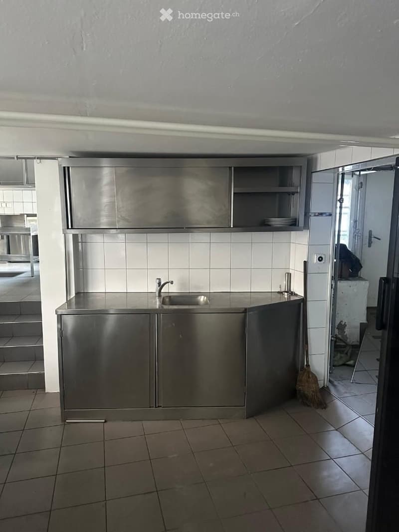Empty kitchen with stainless steel cabinets, a sink, and tiled walls and floor. No furniture or appliances are present.