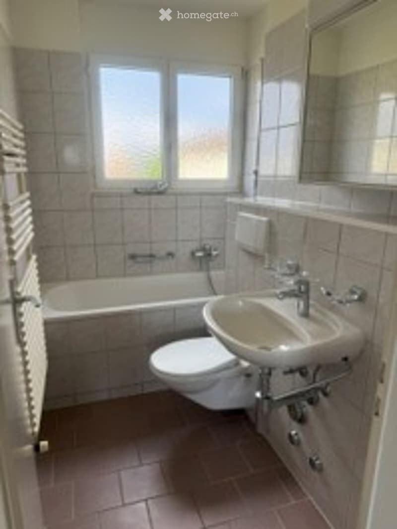 Bathroom with a bathtub, toilet, sink, and radiator. The walls are tiled, and there is a window providing natural light.
