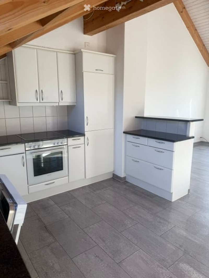 Modern kitchen with white cabinets, stainless steel oven, and black countertops. The space features a tiled floor and exposed wooden beams on the ceiling.