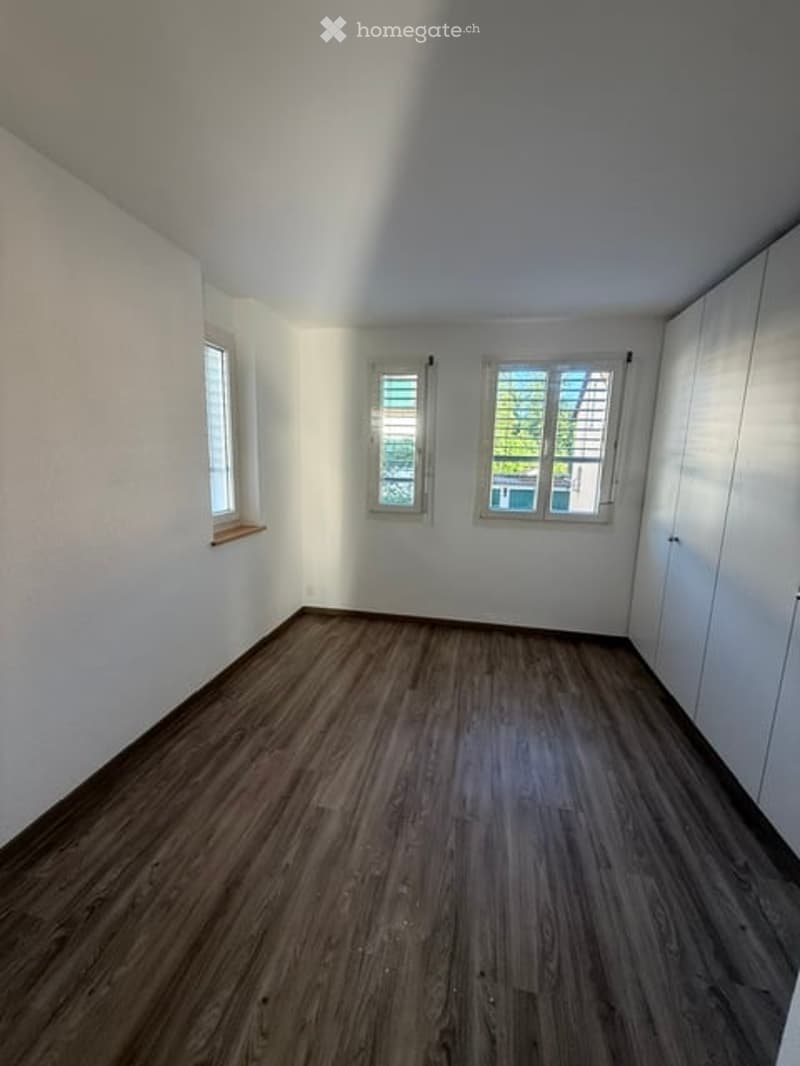 Empty room with wooden flooring, white walls, and three windows with white frames. No furniture or equipment present.