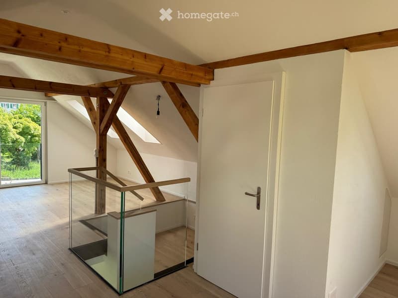 Bright, open hallway with wooden beams, glass railing, and large windows letting in natural light.
