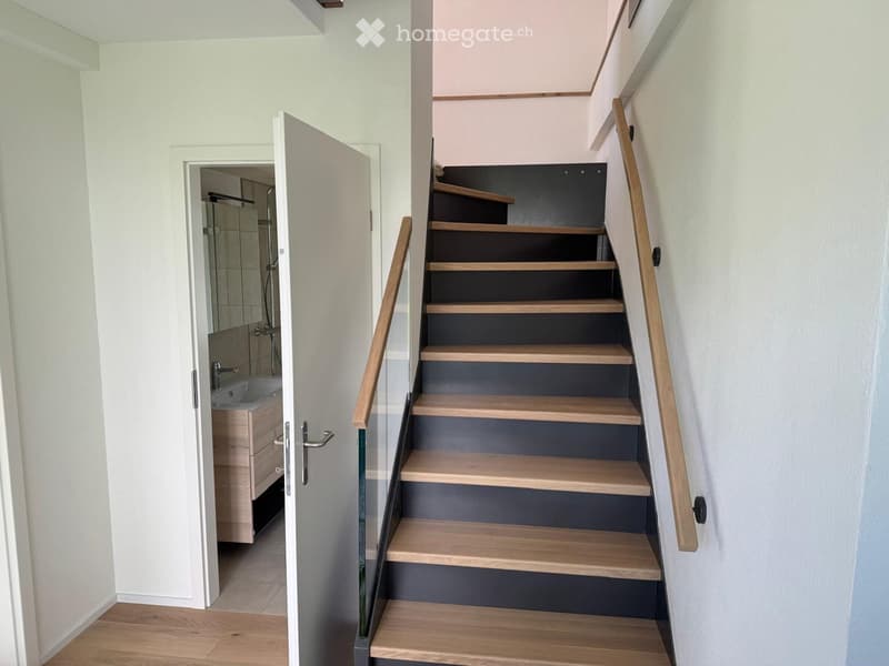 Modern staircase with wooden steps and a glass railing, leading to a bathroom with a sink and mirror.