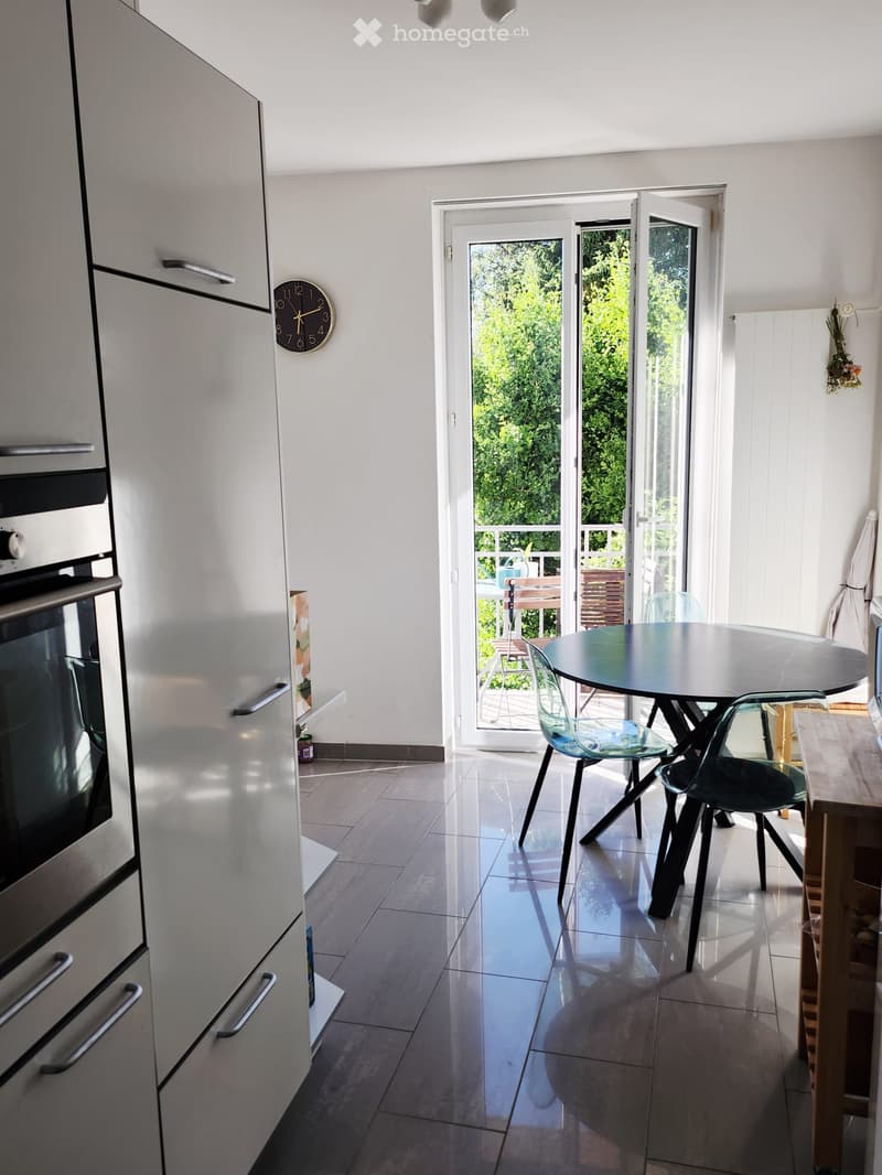 Modern kitchen with white cabinets, a round dining table with chairs, and an open sliding door leading to a balcony.