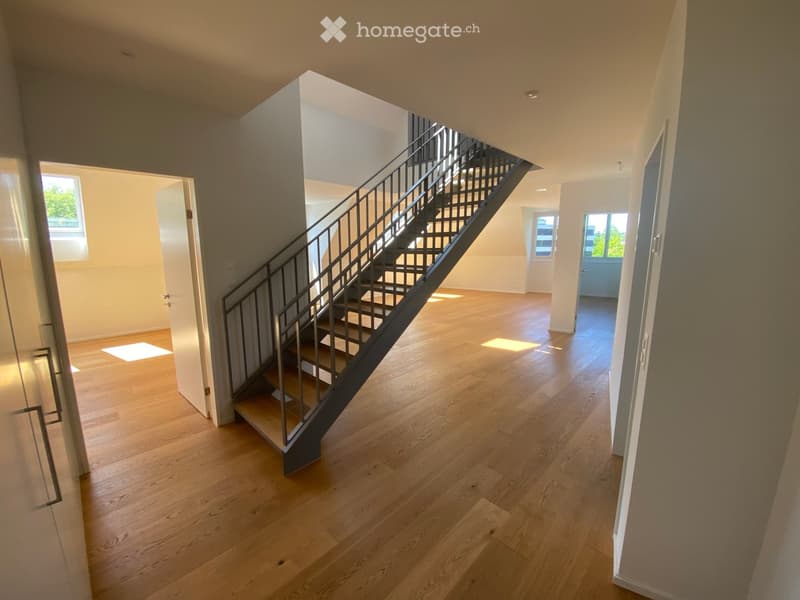 Bright, open hallway with wooden flooring, a staircase leading upwards, and multiple doorways leading to other rooms.